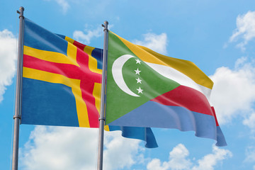 Comoros and Aland Islands flags waving in the wind against white cloudy blue sky together....