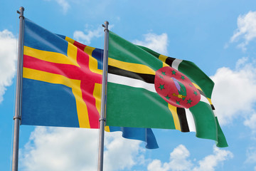 Dominica and Aland Islands flags waving in the wind against white cloudy blue sky together. Diplomacy concept, international relations.