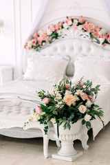 Luxurious white Rococo bed decorated with flowers and a vase with a bouquet in a bright room