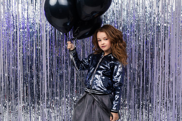 Obraz premium Stylish attractive girl with airy black helium balloons on a background of shiny tinsel. birthday party