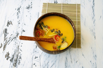 Freshly made creamy pumpkin soup served in coconut bowls with asian seasonings and pumpkin seeds