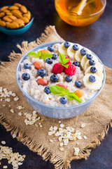 Oatmeal porridge with berries, fruits and honey on dark background. Oatmeal with raspberries, blueberries and almonds on burlap. Healthy breakfast