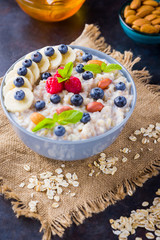 Oatmeal porridge with berries, fruits and honey on dark background. Oatmeal with raspberries, blueberries and almonds on burlap. Healthy breakfast