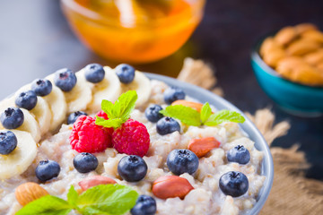 Oatmeal porridge with berries, fruits and honey on dark background. Oatmeal with raspberries, blueberries and almonds on burlap. Healthy breakfast