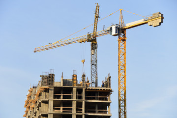 Tower cranes working at construction site against blue sky. Crane lifting a concrete bucket. Construction process of the new residential buildings. Transportation blocks and pouring of the cement mix