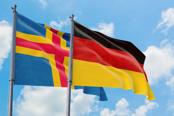Germany and Aland Islands flags waving in the wind against white cloudy blue sky together. Diplomacy concept, international relations.