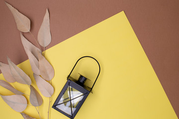 Top view on beige leaves, a cast-iron candlestick in the form of an old lantern on a combined yellow and brown background, place for text