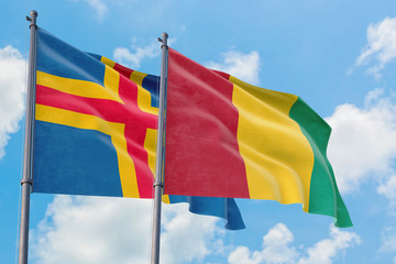 Guinea and Aland Islands flags waving in the wind against white cloudy blue sky together. Diplomacy concept, international relations.