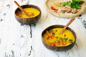 Freshly made creamy pumpkin soup served in coconut bowls with asian seasonings and pumpkin seeds