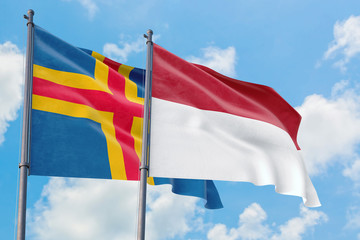 Indonesia and Aland Islands flags waving in the wind against white cloudy blue sky together. Diplomacy concept, international relations.