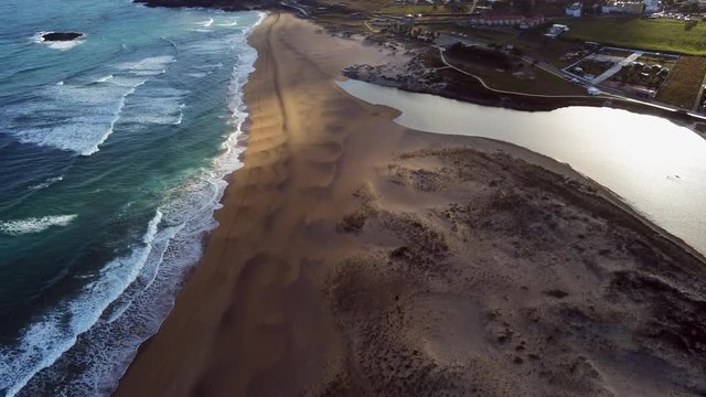 Aerial drone view of Valdovinos sandy golden beach, blue sea, small poddle with a reflection of sun and the moving clouds on it.