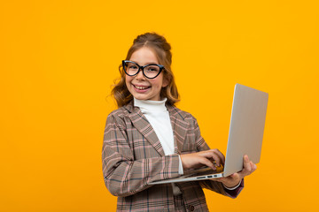 smart caucasian schoolgirl with glasses in a business suit and a jacket with a laptop in hand on a yellow background