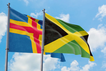 Jamaica and Aland Islands flags waving in the wind against white cloudy blue sky together. Diplomacy concept, international relations.