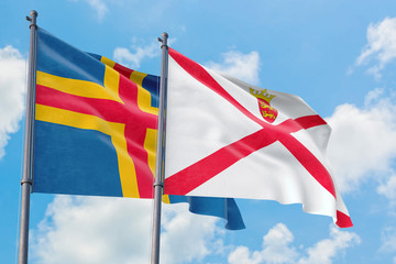 Jersey and Aland Islands flags waving in the wind against white cloudy blue sky together. Diplomacy concept, international relations.