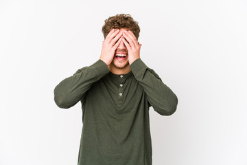 Young blond curly hair caucasian man isolated covers eyes with hands, smiles broadly waiting for a surprise.