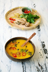 Freshly made creamy pumpkin soup served in coconut bowls with asian seasonings and pumpkin seeds