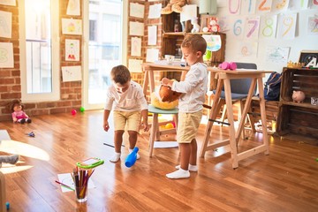 Adorable blonde twins playing using horse toy with stick around lots of toys at kindergarten