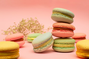 tower of multi-colored bright macaroons close-up, on a pink background, around flowers and cakes
