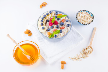 Healthy breakfast. Oatmeal with blueberries, banana and raspberry. Oatmeal with fruits and nuts in a bowl. Cooked oatmeal and honey on white background. Vegetarian food. Copy space
