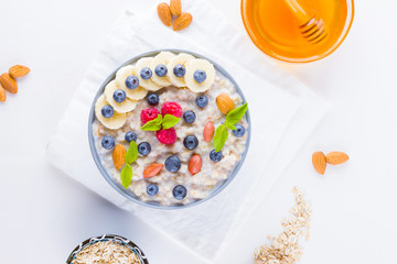Healthy breakfast. Oatmeal with blueberries, banana and raspberry. Oatmeal with fruits and nuts in a bowl. Cooked oatmeal and honey on white background. Vegetarian food. Copy space