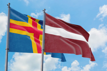 Latvia and Aland Islands flags waving in the wind against white cloudy blue sky together. Diplomacy concept, international relations.