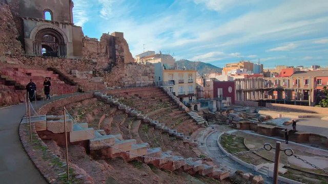 Backward dolly turn reveal panoramic view of amphitheater stage, cityscape in background, Cartagena, Spain