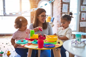 Young beautiful teacher and toddlers playing on the table with lots of toys at kindergarten