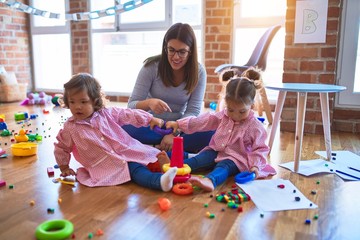 Young beautiful teacher and toddlers wearing uniform building pyramid using hoops at kindergarten