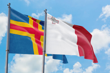 Malta and Aland Islands flags waving in the wind against white cloudy blue sky together. Diplomacy concept, international relations.