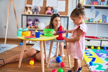 Young beautiful teacher and toddler building pyramid using hoops on the table at kindergarten