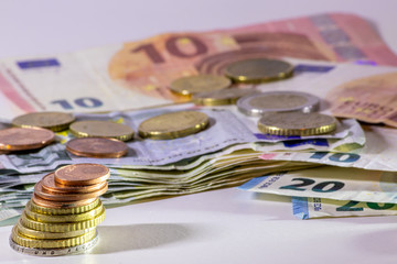 Stapel Euro-Münzen aus 2 Euro, 1 Euro und Cent-Münzen mit einem Haufen Bargeld aus Geldscheinen und EURO-Münzen zeugt von Reichtum in der Finanzwelt und schnelles Geld