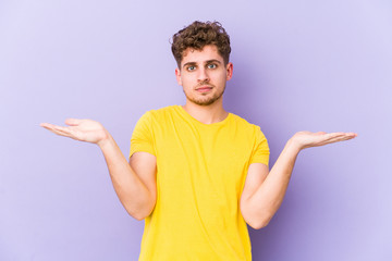 Young blond curly hair caucasian man isolated confused and doubtful shrugging shoulders to hold a copy space.