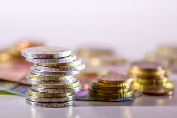 Stapel Euro-Münzen aus 2 Euro, 1 Euro und Cent-Münzen mit einem Haufen Bargeld aus Geldscheinen und EURO-Münzen zeugt von Reichtum in der Finanzwelt und schnelles Geld