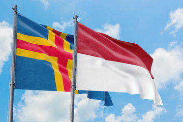 Monaco and Aland Islands flags waving in the wind against white cloudy blue sky together. Diplomacy concept, international relations.