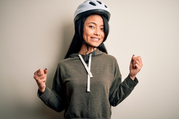 Young beautiful chinese woman wearing bike helmet over isolated white background celebrating surprised and amazed for success with arms raised and open eyes. Winner concept.