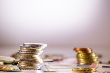 Stapel Euro-Münzen aus 2 Euro, 1 Euro und Cent-Münzen mit einem Haufen Bargeld aus Geldscheinen und EURO-Münzen zeugt von Reichtum in der Finanzwelt und schnelles Geld