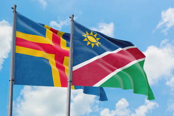 Namibia and Aland Islands flags waving in the wind against white cloudy blue sky together. Diplomacy concept, international relations.