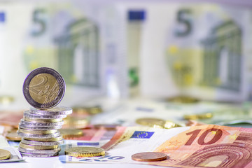 Stapel Euro-Münzen aus 2 Euro, 1 Euro und Cent-Münzen mit einem Haufen Bargeld aus Geldscheinen und EURO-Münzen zeugt von Reichtum in der Finanzwelt und schnelles Geld