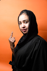 young beautiful Muslim girl wearing Hijab showing and lifting a finger in sign of the best on orange background , girl in Arabic Traditional Abbaya