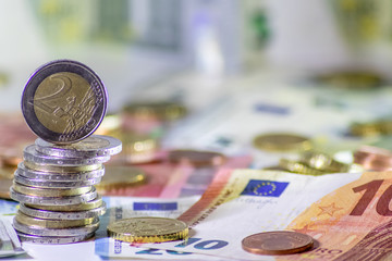 Stapel Euro-Münzen aus 2 Euro, 1 Euro und Cent-Münzen mit einem Haufen Bargeld aus Geldscheinen und EURO-Münzen zeugt von Reichtum in der Finanzwelt und schnelles Geld
