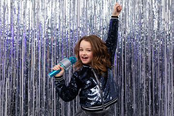 positive stylish girl singing with a microphone in her hands and a raised hand up on a shiny tinsel background