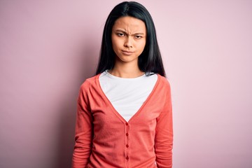 Young beautiful chinese woman wearing casual sweater over isolated pink background skeptic and...