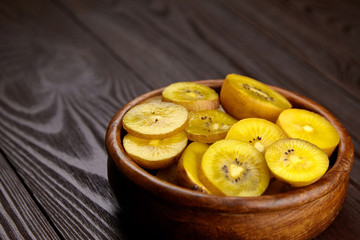 Kiwi Gold fruit slices in wooden bowl. Sliced kiwi with yellow flesh in salad dish on brown background. Juicy ripe healthy fruit