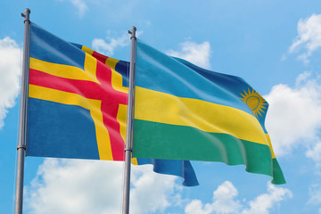 Rwanda and Aland Islands flags waving in the wind against white cloudy blue sky together. Diplomacy concept, international relations.