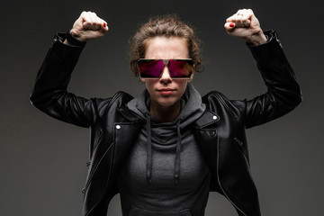 black friday concept. attractive caucasian girl in a black leather jacket and gray sweatshirt holds her hands up with fists, showing strength on a dark gray background