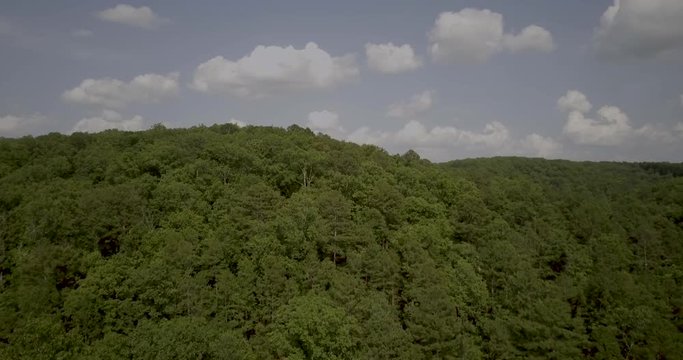 Ascending aerial drone shot of trees, slowly revealing hills and mountains on the horizon in south Missouri.