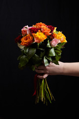 Bouquet of different color roses in female hand on a black background. Red, orange and pink flowers. Romantic Valentine's Day Gift