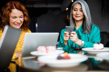 Charming women using laptop and cellphone in cafe