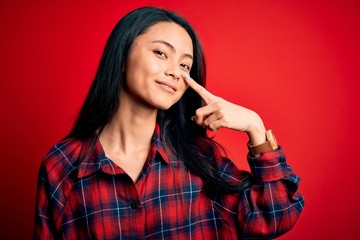 Young beautiful chinese woman wearing casual shirt over isolated red background Pointing with hand finger to face and nose, smiling cheerful. Beauty concept