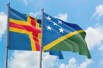 Solomon Islands and Aland Islands flags waving in the wind against white cloudy blue sky together. Diplomacy concept, international relations.